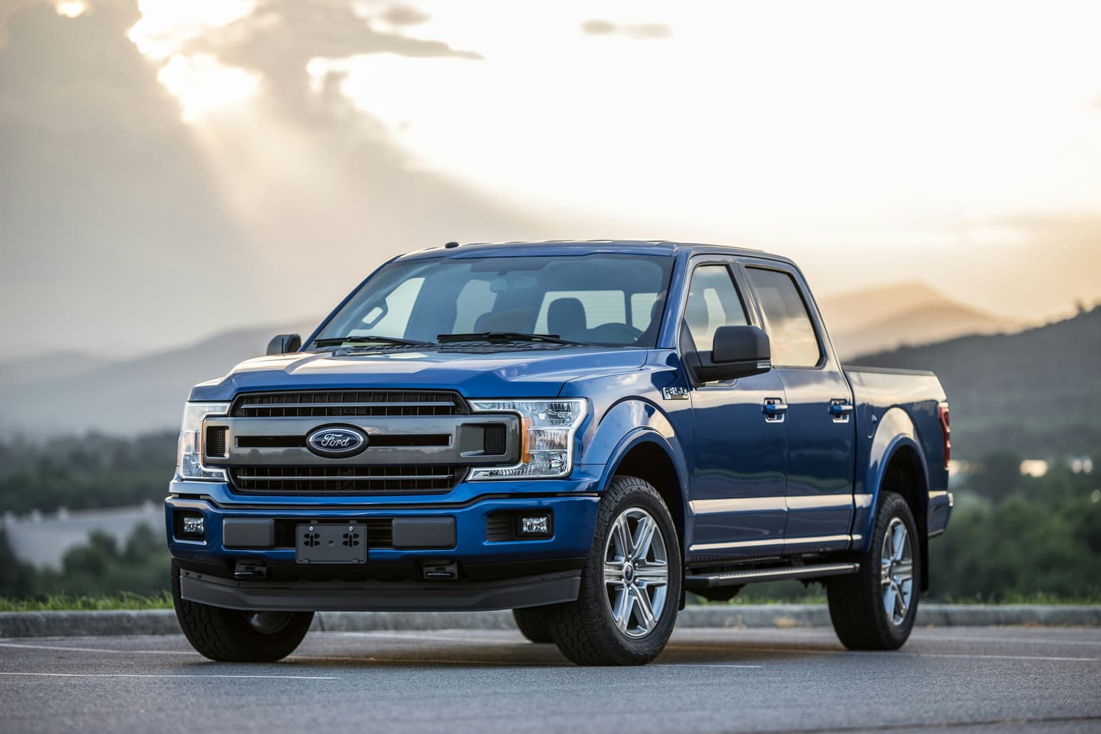 Blue Ford F-150 pickup truck at sunset with mountains in background