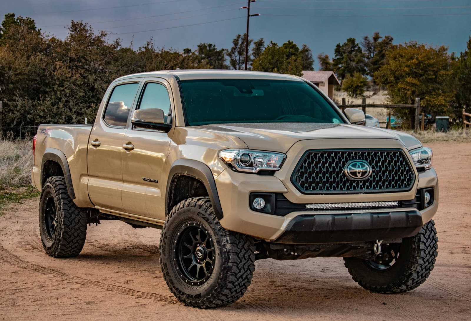Tan Toyota Tacoma lifted truck with off-road tires on a dirt road