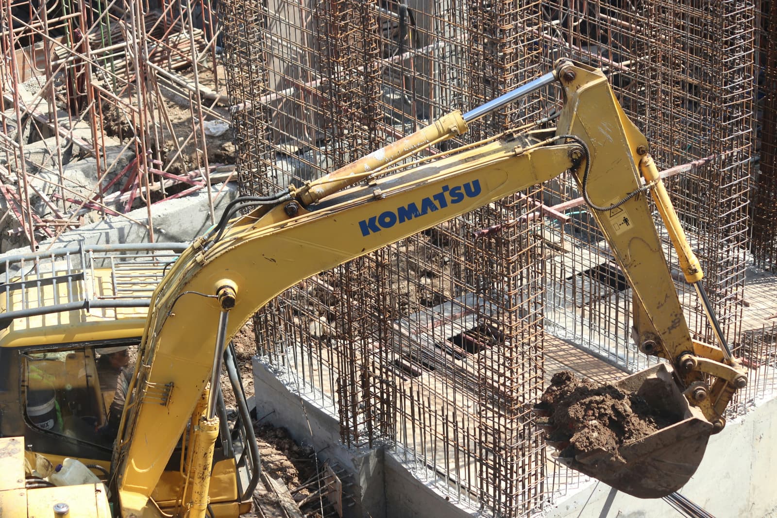 Yellow excavator digging at a construction site with steel rebar reinforcement