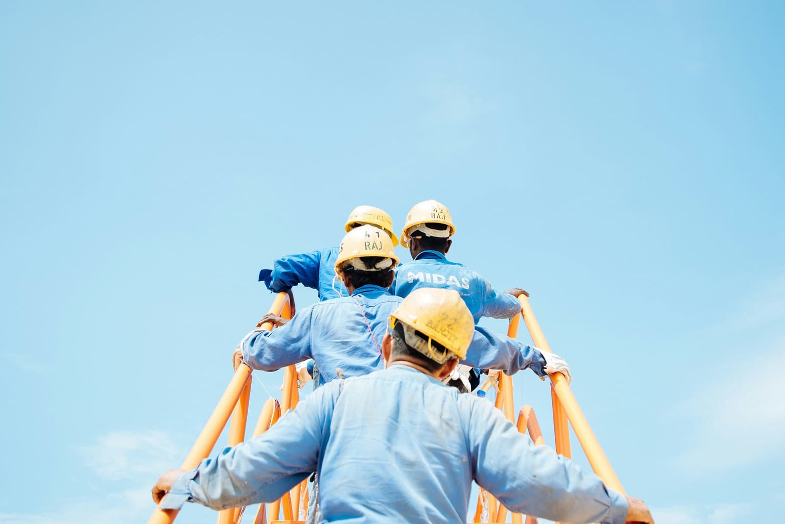 Three construction workers in blue uniforms and hard hats climbing a ladder on a job site