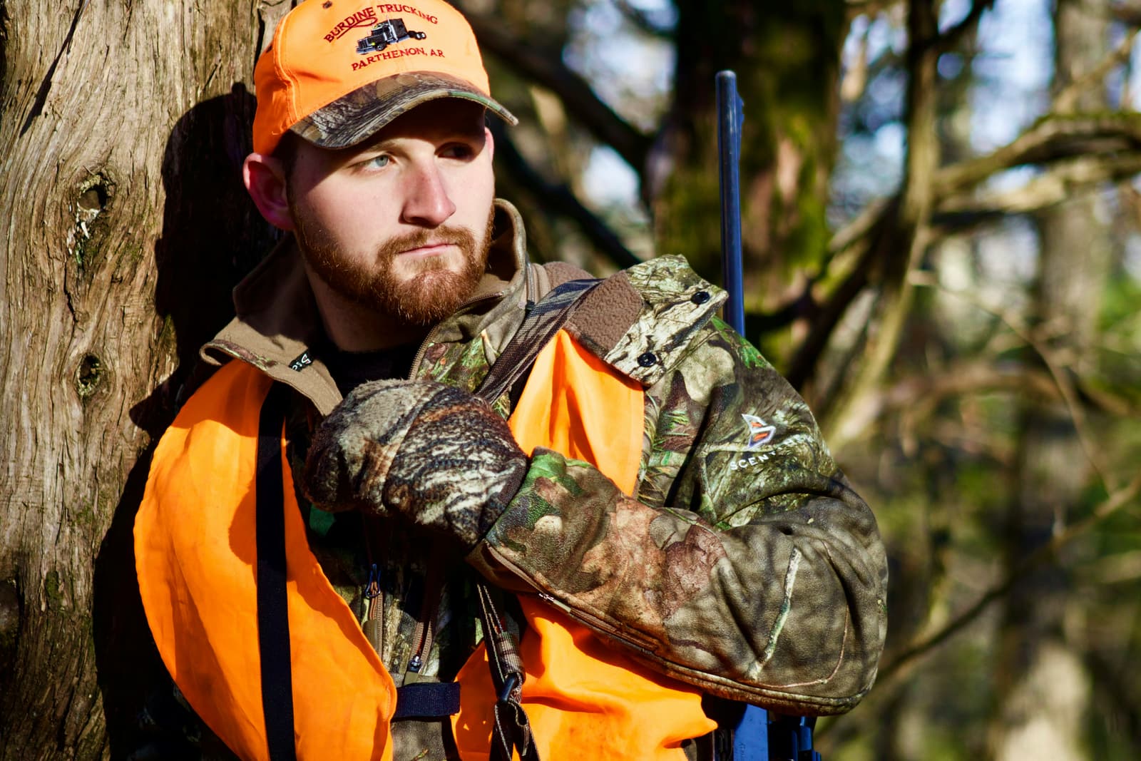 Young hunter in orange safety vest leaning against a tree in the woods