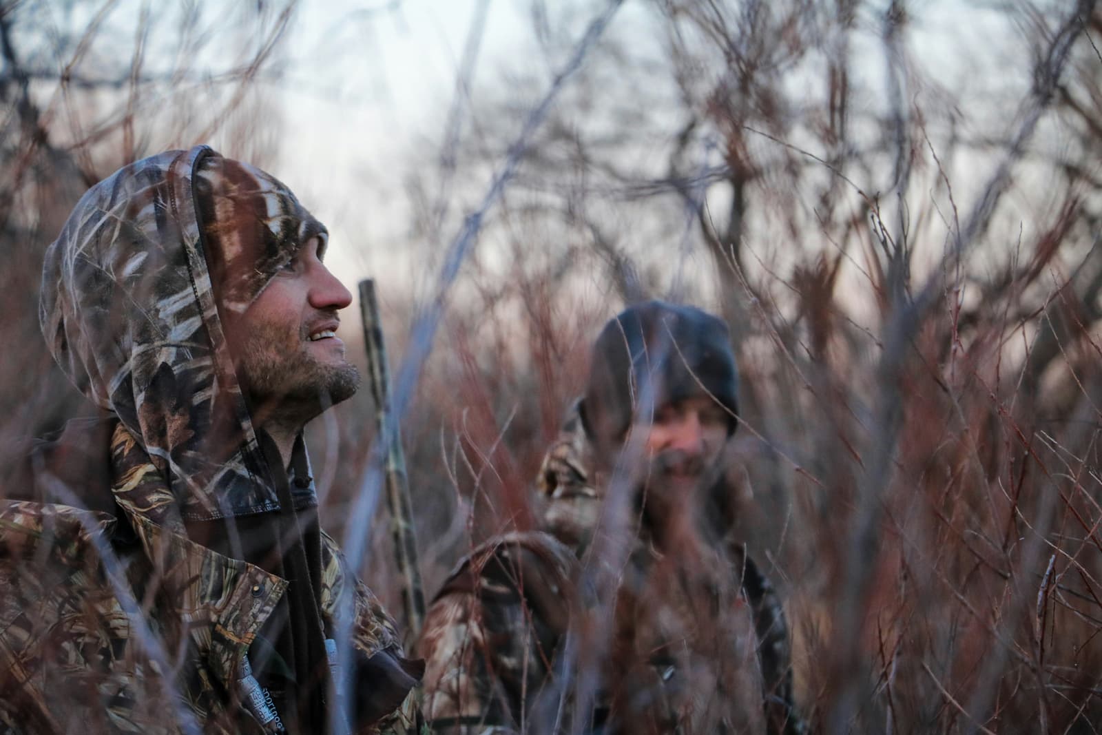 Two hunters in camouflage concealed in thick brush on a hunt