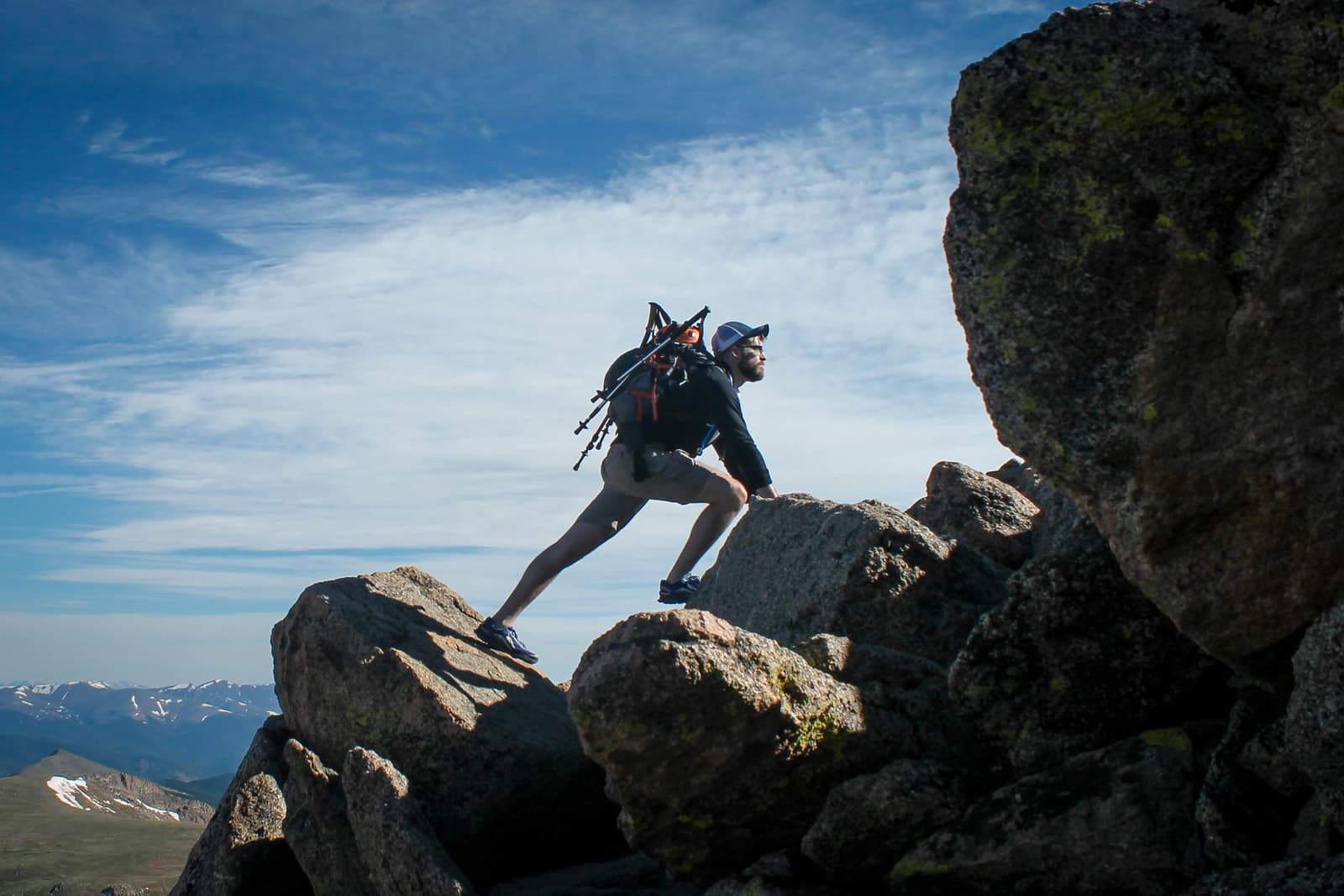 Man scrambling over boulders with hiking backpack against blue sky