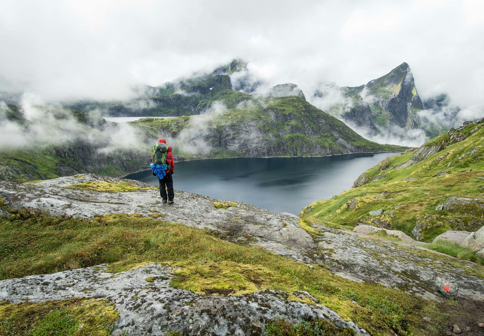Hiker overlooking a misty mountain fjord and alpine lake
