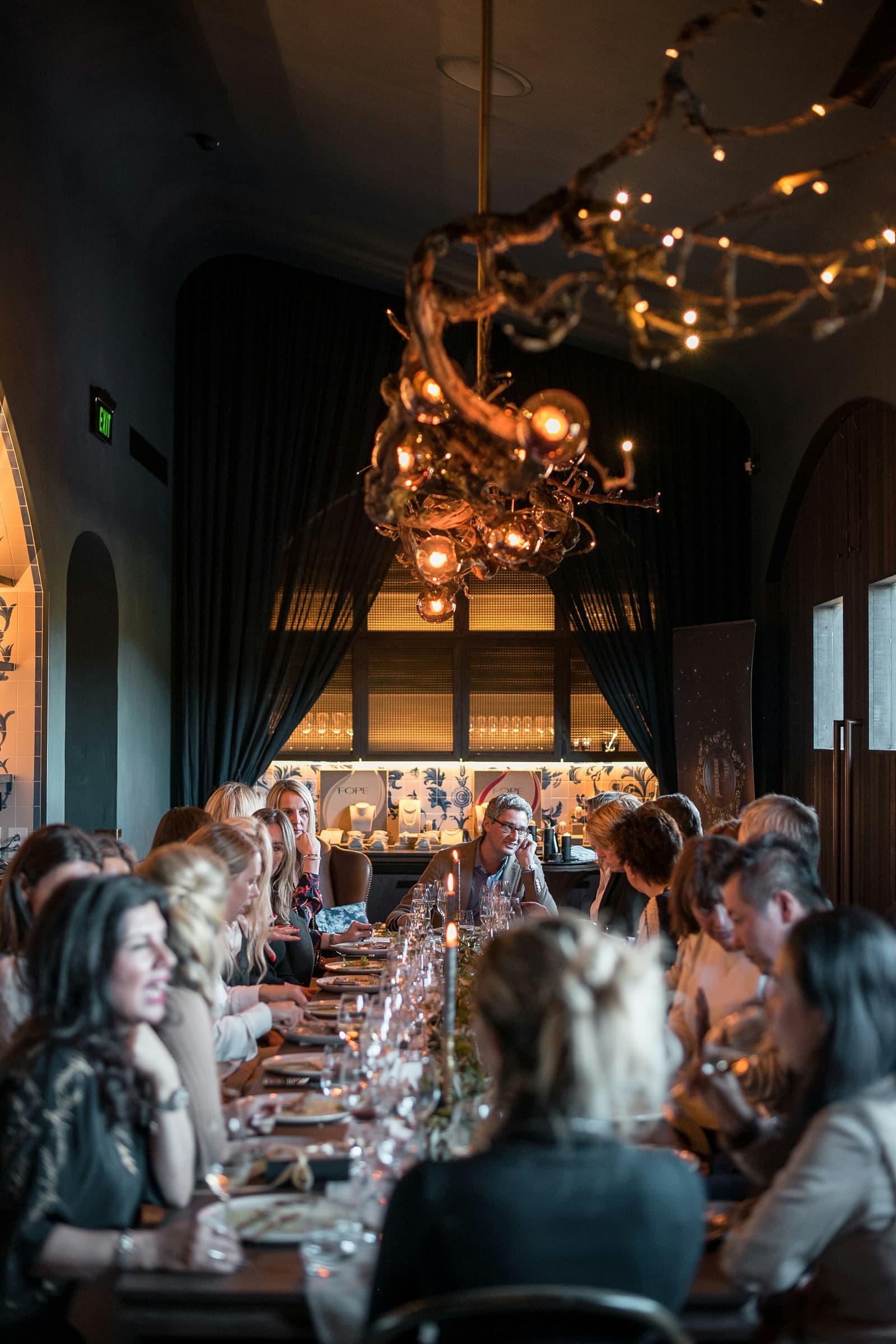 Elegant restaurant dining room with ornate chandelier and guests seated at a long candlelit table